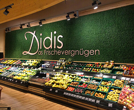 Echte Mooswand für Shoppingvergnügen Evergreen Moos Standard, vorgesetzter Schriftzug 'Didis Frischevergnügen' in der Obst- und Gemüseabteilung